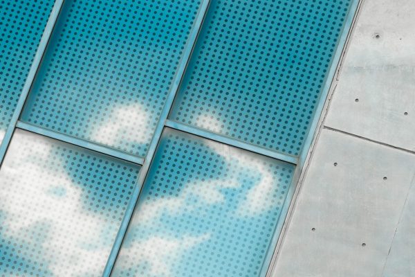 Cloud reflections on perforated glass windows with concrete wall contrast.